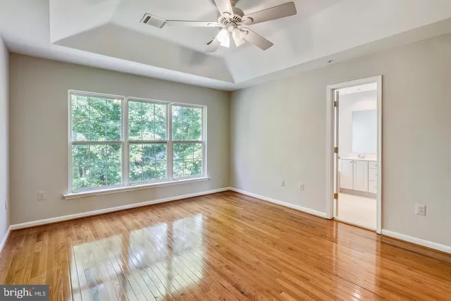 an empty room with wooden floor fan and windows