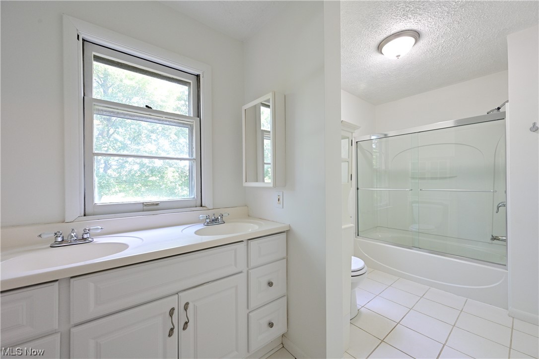 8280 Lafayette Road Lodi, OH 44254 - Photo 26 of 35 Full bathroom with light tile floors, dual bowl vanity, shower / bath combination with glass door, and a textured ceiling