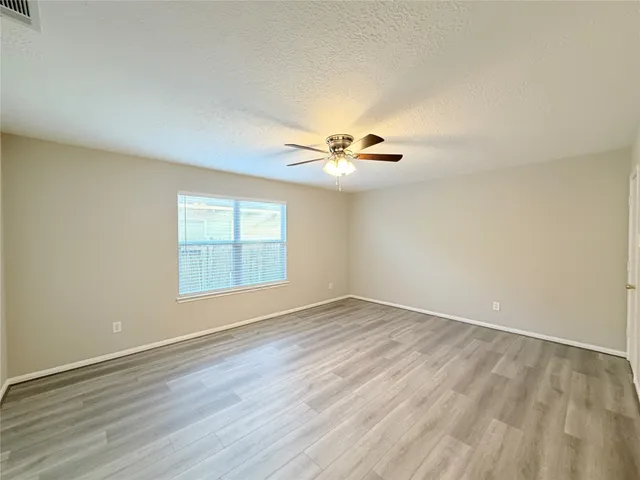 an empty room with wooden floor fan and windows