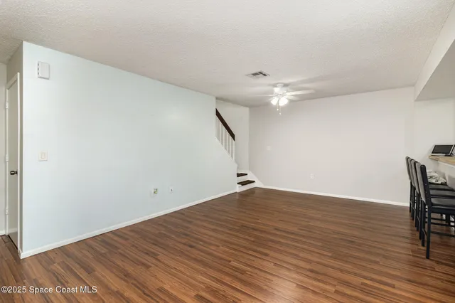 a view of an empty room with wooden floor and a ceiling fan