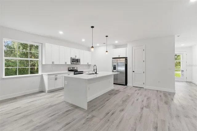 a large white kitchen with wooden floors stainless steel appliances and white cabinets