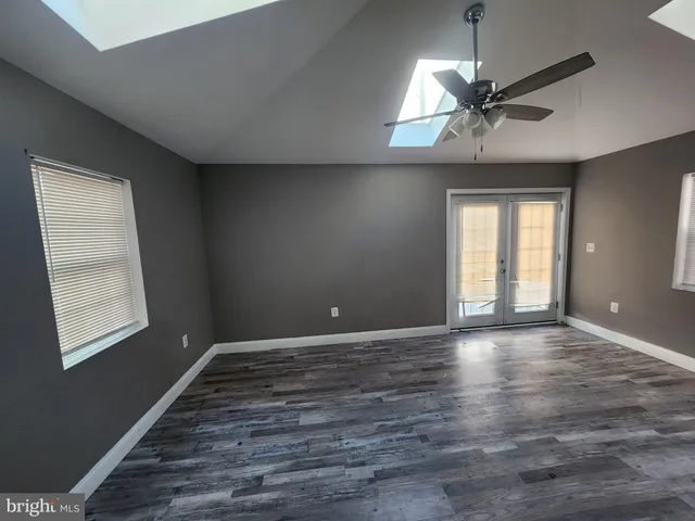 an empty room with wooden floor windows and fan