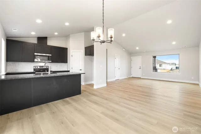 a kitchen with stainless steel appliances kitchen island granite countertop a refrigerator a stove a sink and a microwave with wooden floor