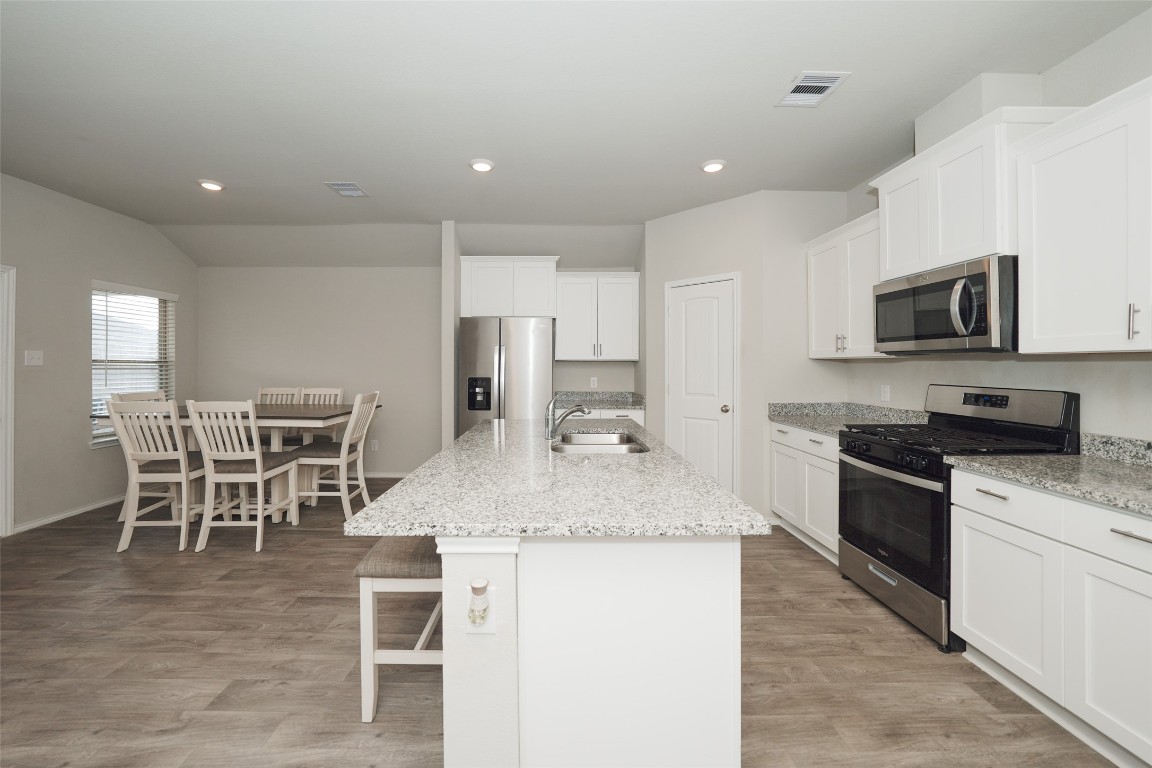 a kitchen with stainless steel appliances granite countertop a stove top oven a sink a dining table and chairs