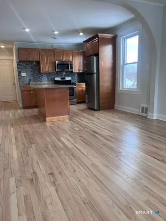 a view of kitchen with stainless steel appliances granite countertop a refrigerator stove a sink dishwasher and wooden floor