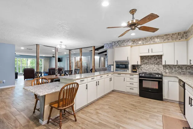 a kitchen with stainless steel appliances granite countertop a stove top oven a sink a dining table and chairs with wooden floor