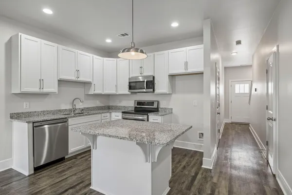 a kitchen with kitchen island granite countertop a stove a sink a refrigerator and white cabinets with wooden floor