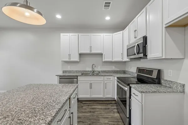 a kitchen with stainless steel appliances granite countertop a stove top oven a sink dishwasher and a microwave oven with white cabinets