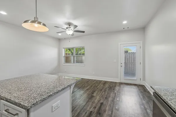 an empty room with wooden floor chandelier fan and kitchen view