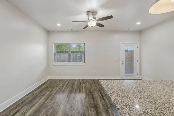 an empty room with wooden floor ceiling fan and windows
