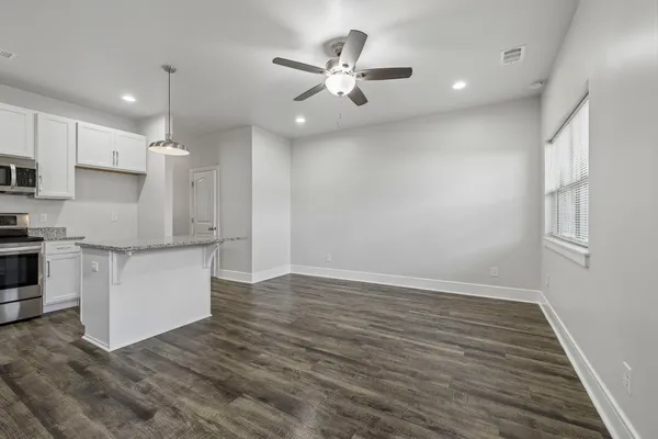 a view of an empty room with kitchen appliances and a ceiling fan