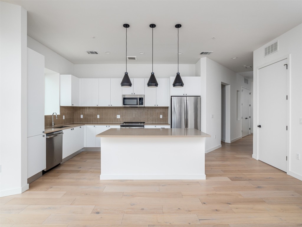 800 Embassy Drive, Unit 237 Austin, TX 78702 - Photo 4 of 35 Kitchen featuring pendant lighting, white cabinets, backsplash, a center island, and appliances with stainless steel finishes