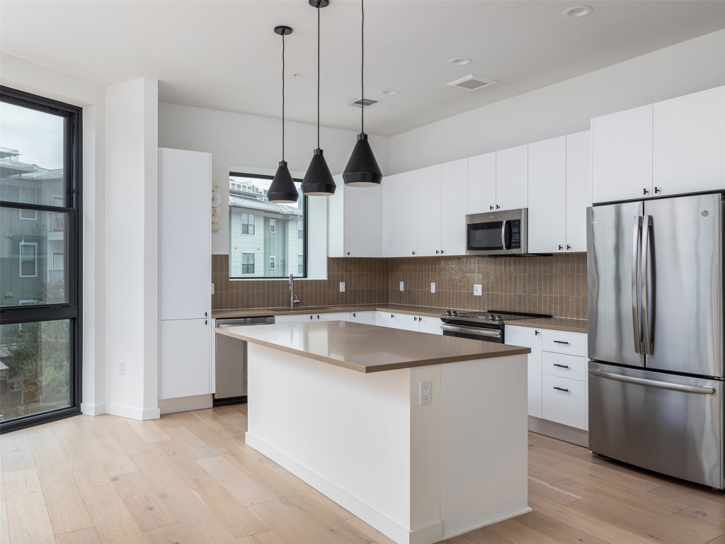 800 Embassy Drive, Unit 237 Austin, TX 78702 - Photo 5 of 35 Kitchen featuring stainless steel appliances, white cabinets, hanging light fixtures, and light wood-style floors