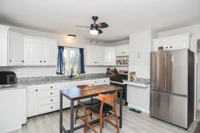 a kitchen with granite countertop a refrigerator a stove a sink and white cabinets with wooden floor