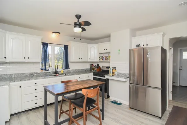 a kitchen with granite countertop a refrigerator a stove a sink and white cabinets with wooden floor