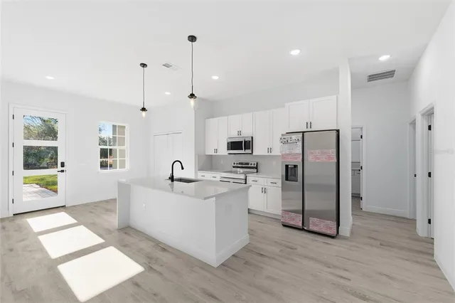 a kitchen with stainless steel appliances kitchen island granite countertop a refrigerator a sink a stove and white cabinets with wooden floor