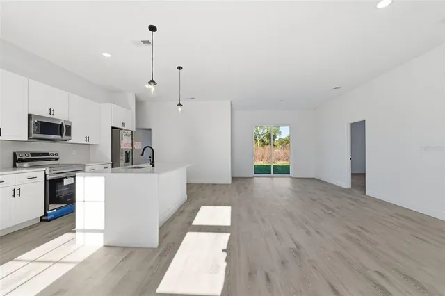 a living room with stainless steel appliances kitchen island granite countertop a refrigerator a stove top oven a sink and dishwasher with wooden floor
