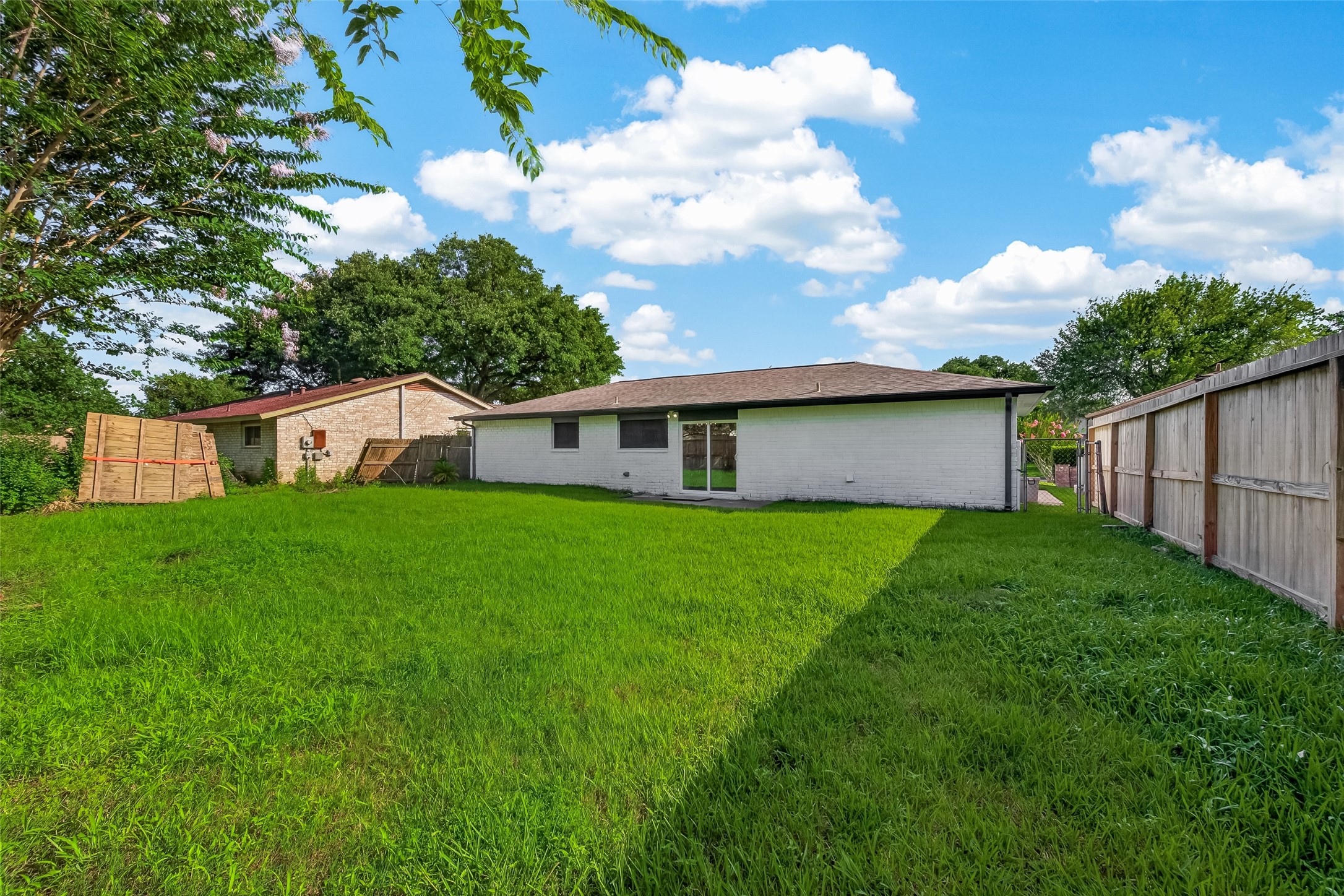 16619 Tibet Road Friendswood, TX 77546 - Photo 26 of 29 Spacious backyard with lush green grass, bordered by a wooden fence for privacy. The rear of the house is visible, featuring a simple, single-story design with large windows. Ideal for outdoor activities and relaxation.