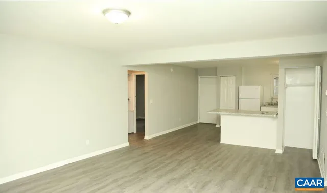 a view of an empty room and kitchen with wooden floor