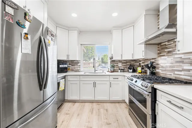 a kitchen with stainless steel appliances granite countertop a stove a sink dishwasher a refrigerator and white cabinets with wooden floor