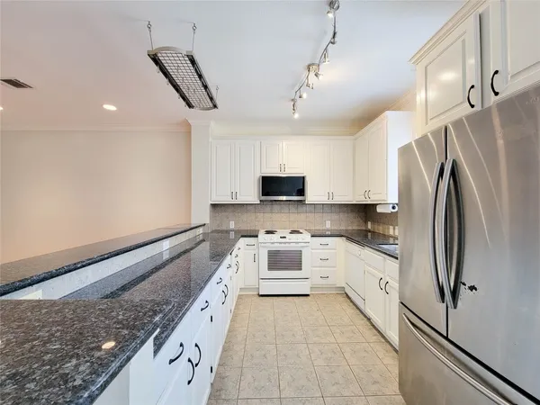 a large kitchen with stainless steel appliances granite countertop a refrigerator sink and white cabinets