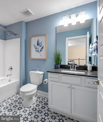 a bathroom with a granite countertop sink a toilet a mirror a vanity a lamp and bathtub