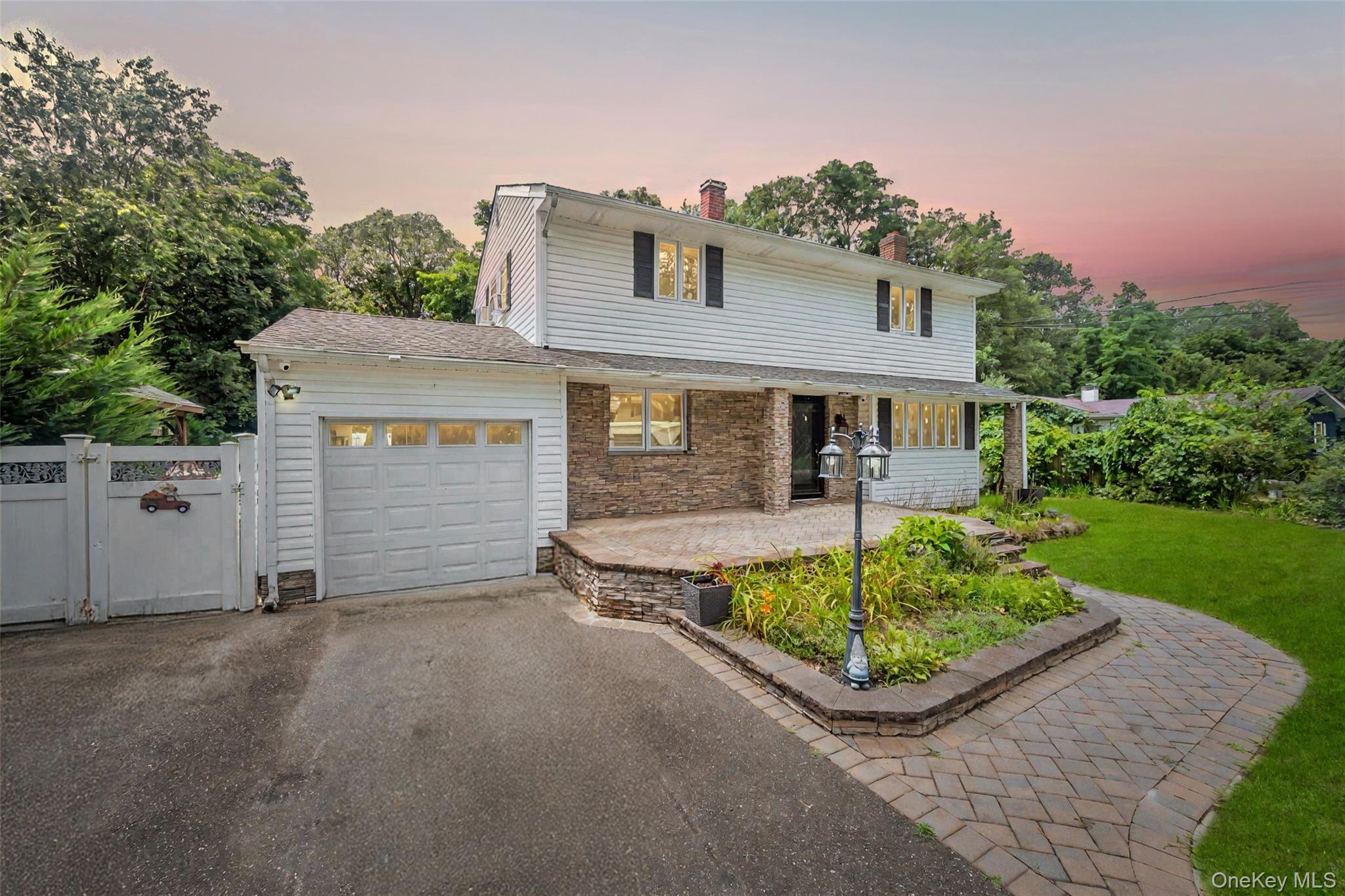 Traditional-style home with a garage, asphalt driveway, stone siding, a gate, and a chimney