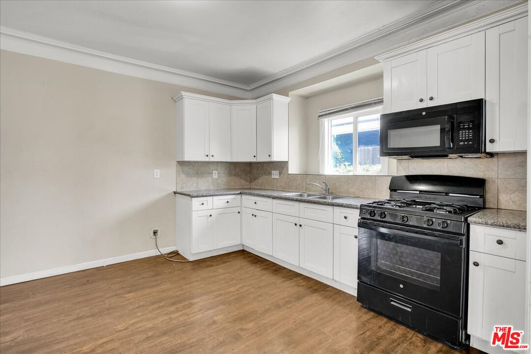 1221 West 152nd Street Compton, CA 90220 - Photo 6 of 20 a kitchen with granite countertop a stove top oven a sink dishwasher and white cabinets with wooden floor