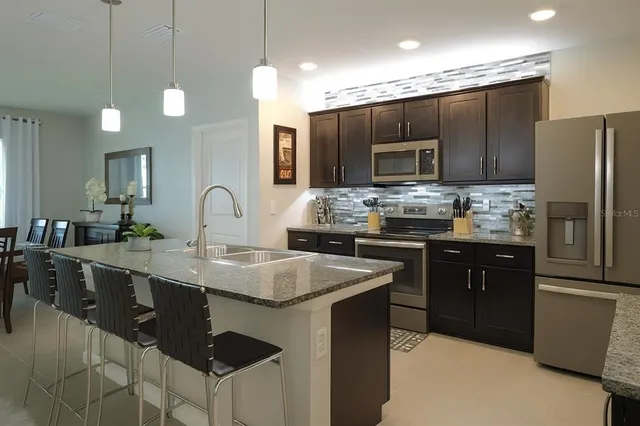 a kitchen with kitchen island granite countertop stainless steel appliances a sink a stove a refrigerator a center island and chairs