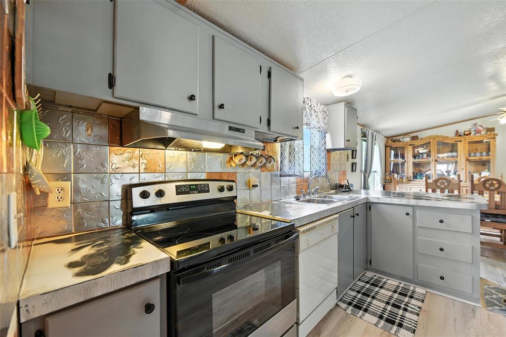 1933 Carter Road Springtown, TX 76082 - Photo 13 of 38 Kitchen with stainless steel electric stove, a peninsula, under cabinet range hood, tasteful backsplash, and white dishwasher