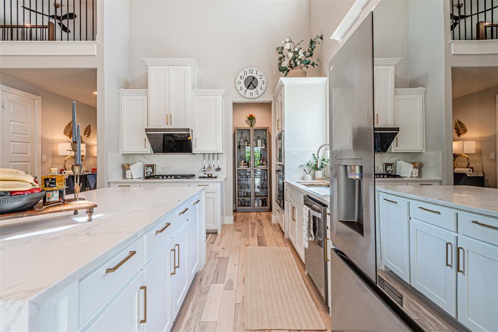 1070 Adair Road Prosper, TX 75078 - Photo 9 of 40 Spacious kitchen featuring an expansive island with a stone-finish countertop, high vaulted ceilings, light wood-finish flooring, white cabinetry with gold-tone hardware, and stainless steel appliances