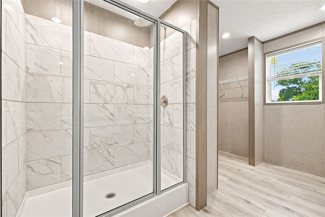 112 Purdy Road Iva, SC 29655 - Photo 16 of 33 Marble-patterned tile lines the walk-in shower adjacent to a spacious closet with wood-look flooring.