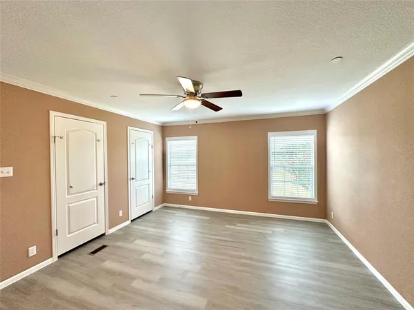 an empty room with wooden floor chandelier fan and windows