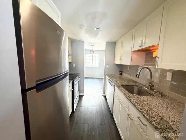 a kitchen with stainless steel appliances granite countertop a refrigerator a stove and a sink with wooden floor