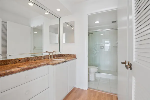 a bathroom with a granite countertop sink a toilet a mirror and shower