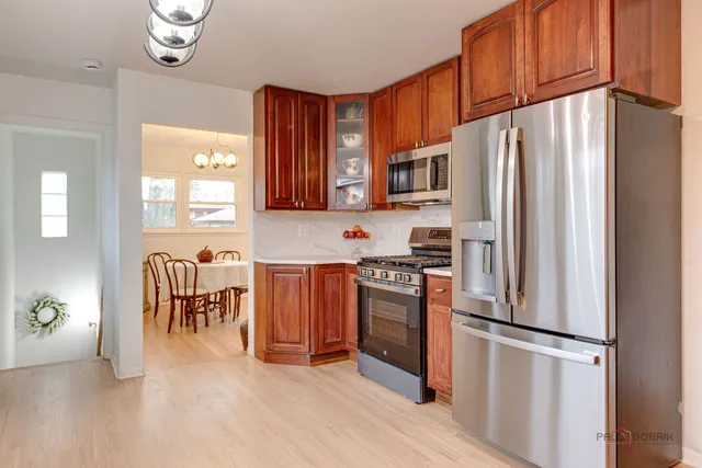 a kitchen with stainless steel appliances a refrigerator a stove a sink a dining table and chairs with wooden floor