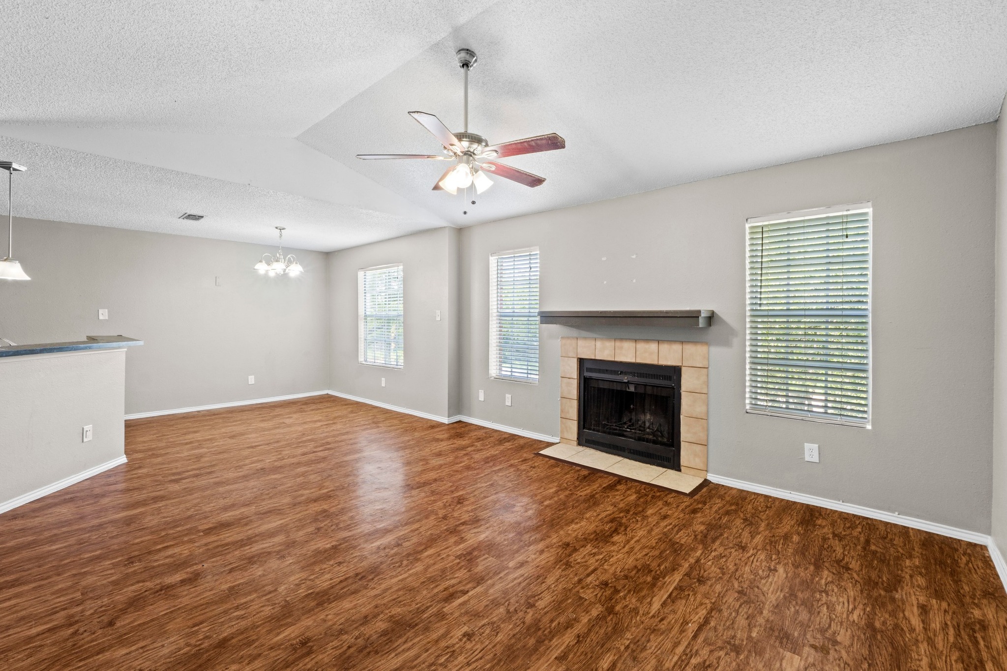 4208 Duval Road, Unit C Austin, TX 78759 - Photo 3 of 28 Unfurnished living room featuring a tile fireplace, wood finished floors, a ceiling fan, a chandelier, and a textured ceiling