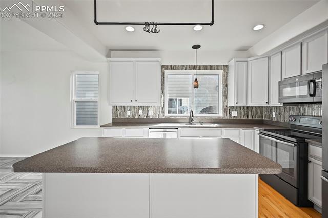 10165 Angeles Road Peyton, CO 80831 - Photo 13 of 38 Kitchen featuring white cabinetry, backsplash, electric range, sink, and a center island