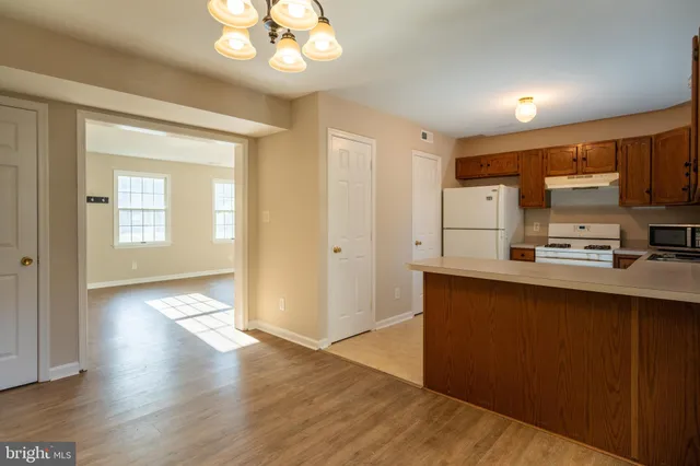 a kitchen with stainless steel appliances granite countertop a refrigerator a sink dishwasher a stove and white cabinets with wooden floor