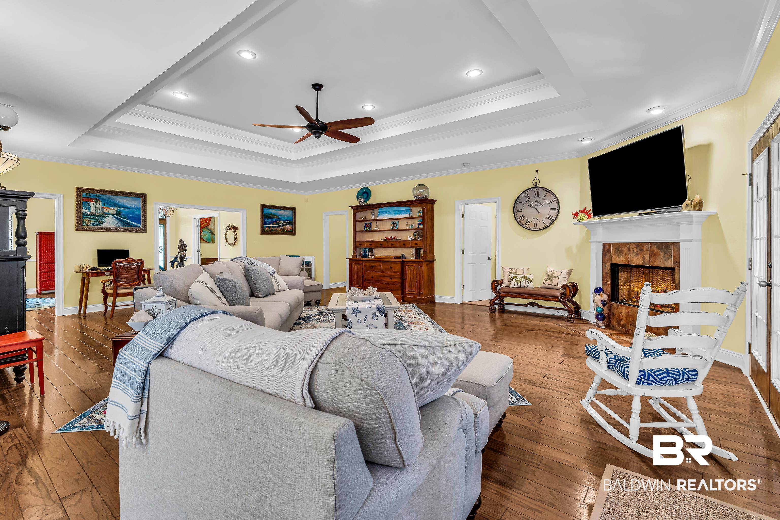 7014 Blakeley Road Daphne, AL 36527 - Photo 24 of 45 Spacious living area featuring wood-finish flooring, a tray ceiling with recessed lighting and a ceiling fan, a fireplace with a white mantel and stone surround, and light-colored walls