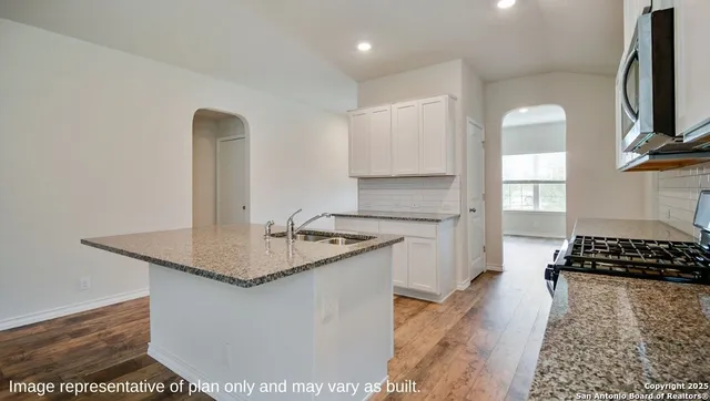 a kitchen with kitchen island granite countertop a sink cabinets and wooden floor