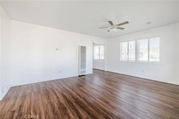 an empty room with wooden floor ceiling fan and windows