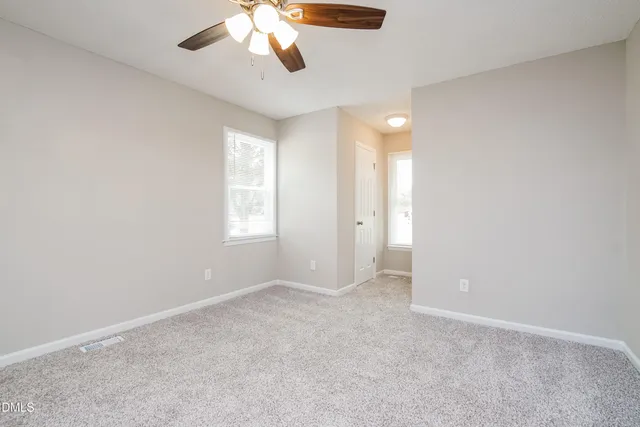 an empty room with chandelier fan and windows