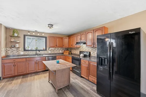 a kitchen with stainless steel appliances granite countertop a refrigerator a sink dishwasher a stove and white countertops with wooden floor