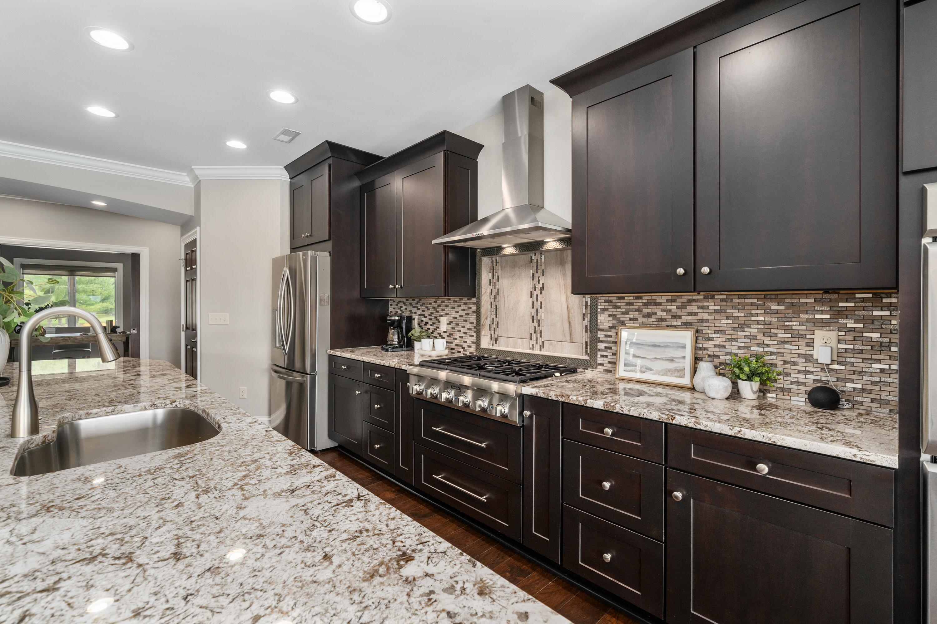 4640 Maynard Road Delaware, OH 43015 - Photo 12 of 91 Gourmet kitchen featuring dark wood cabinetry, stainless steel appliances, a mosaic tile backsplash, and light-toned, speckled countertops with an undermount sink