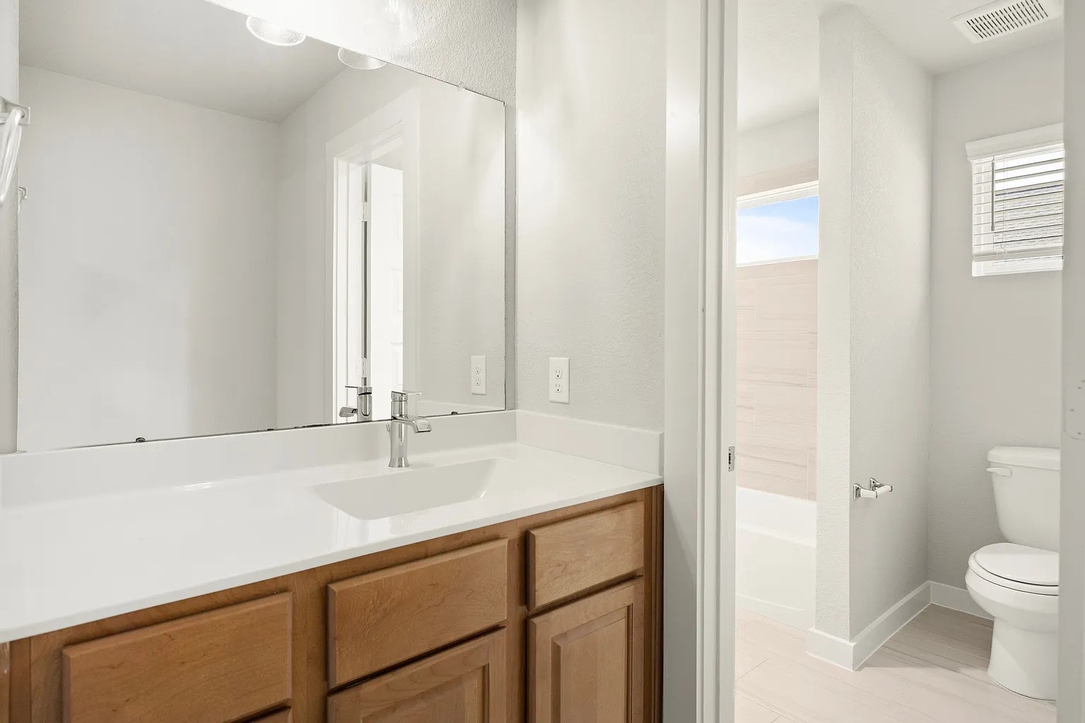 3018 North Spring Drive Spring, TX 77373 - Photo 25 of 25 Bright and modern bathroom featuring a spacious vanity with a sleek countertop, ample cabinetry, and a large mirror. The adjoining area includes a well-lit toilet and shower space, complemented by natural light from a window.