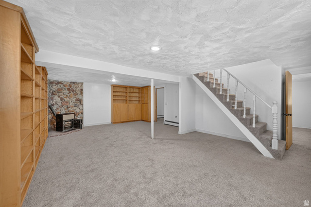 220 East Greenwood Avenue Midvale, UT 84047 - Photo 24 of 46 Spacious carpeted room featuring a stone accent wall, built-in shelving, a built-in wood stove, a staircase with white spindles, and recessed lighting