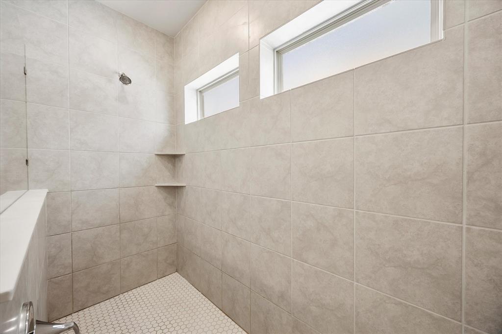 9224 Lamar Street Rowlett, TX 75089 - Photo 14 of 27 Shower featuring large format wall tiling, a hex tile floor, two corner shelves, a shower head fixture, and two transom windows