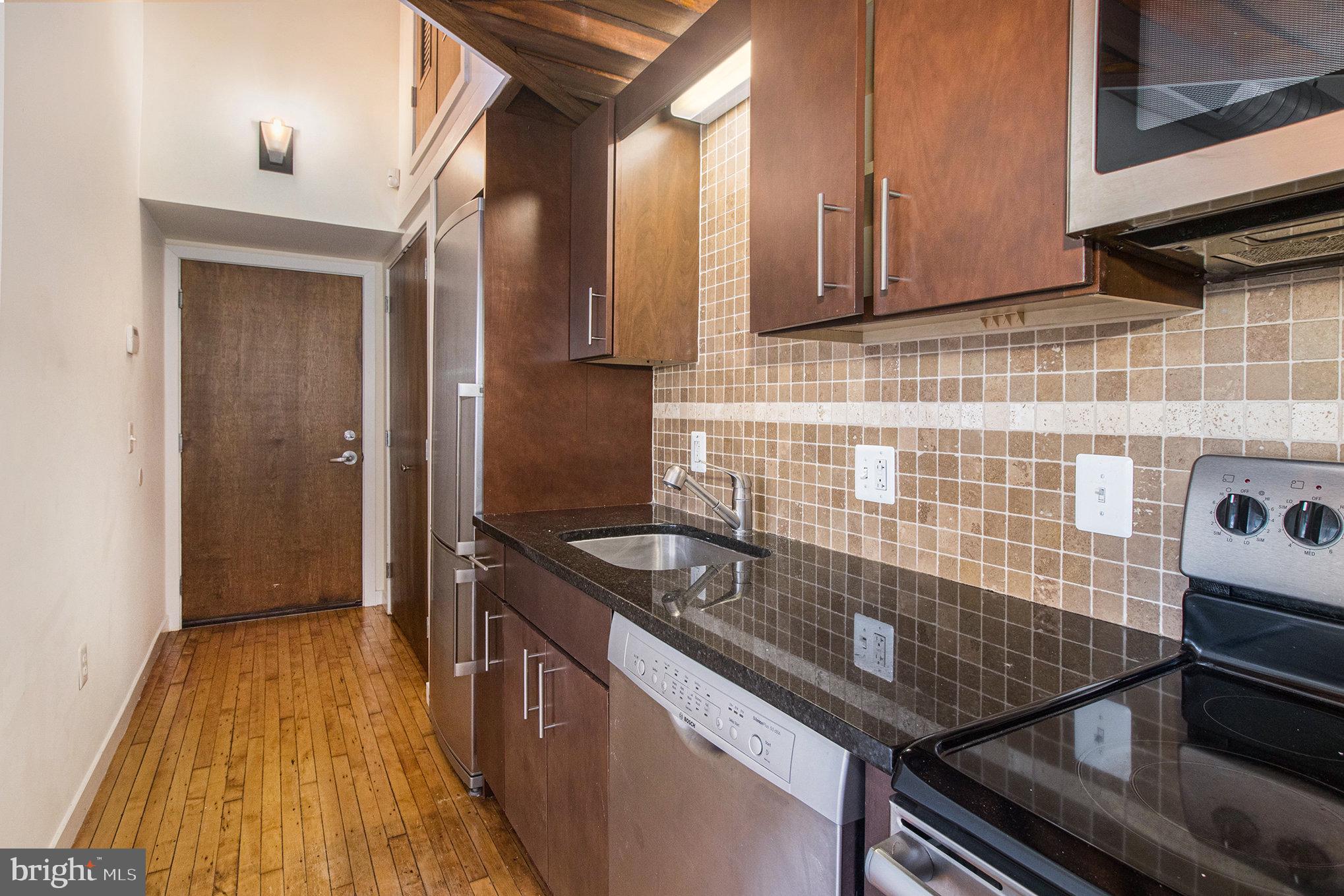 1201 Fitzwater Street, Unit 207 Philadelphia, PA 19147 - Photo 18 of 39 a kitchen with granite countertop a sink a stove and wooden cabinets