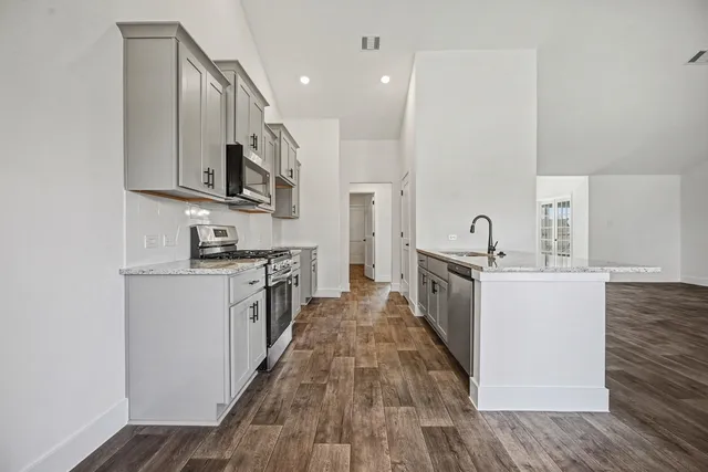 a large kitchen with stainless steel appliances a large counter top a stove a sink and a refrigerator